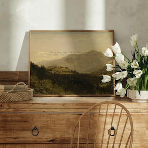 May include: A framed print with a quote by the author, "Only one life, twill soon be past, Only what's done for Christ will last." The print features a landscape painting of a mountain range with trees and a cloudy sky. The print is sitting on a wooden table with a vase of white tulips.
