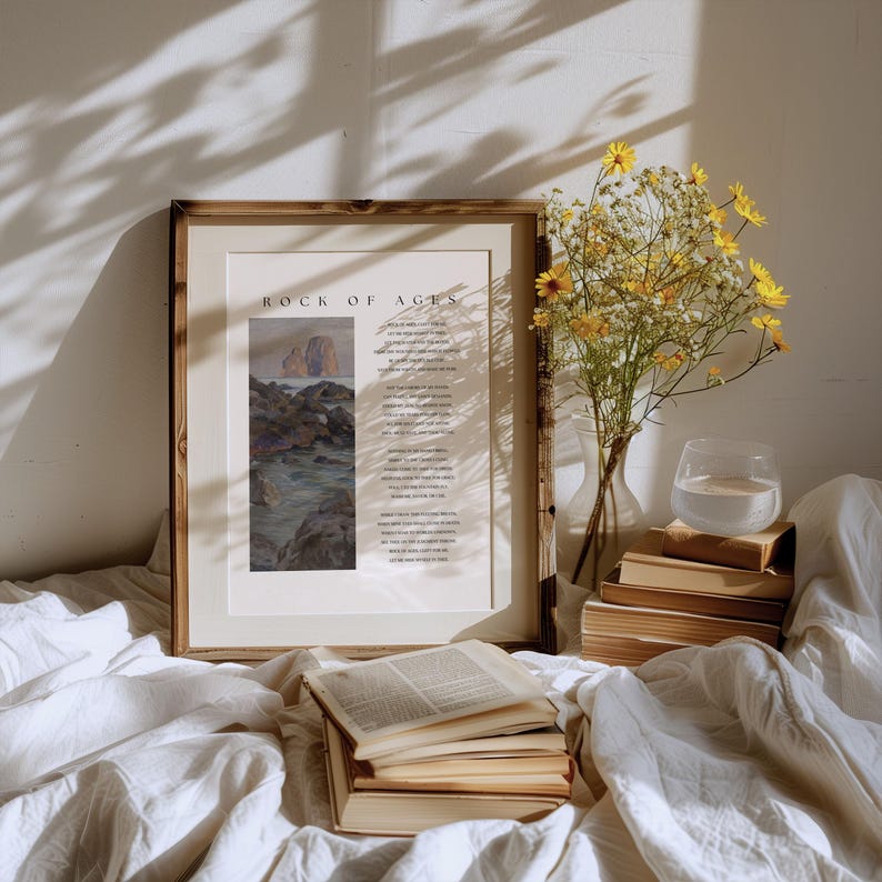 May include: A framed print with the text "ROCK OF AGES" and a landscape painting. A vase of yellow flowers, a glass of water, and a stack of books are on a white surface. The scene is bathed in sunlight.