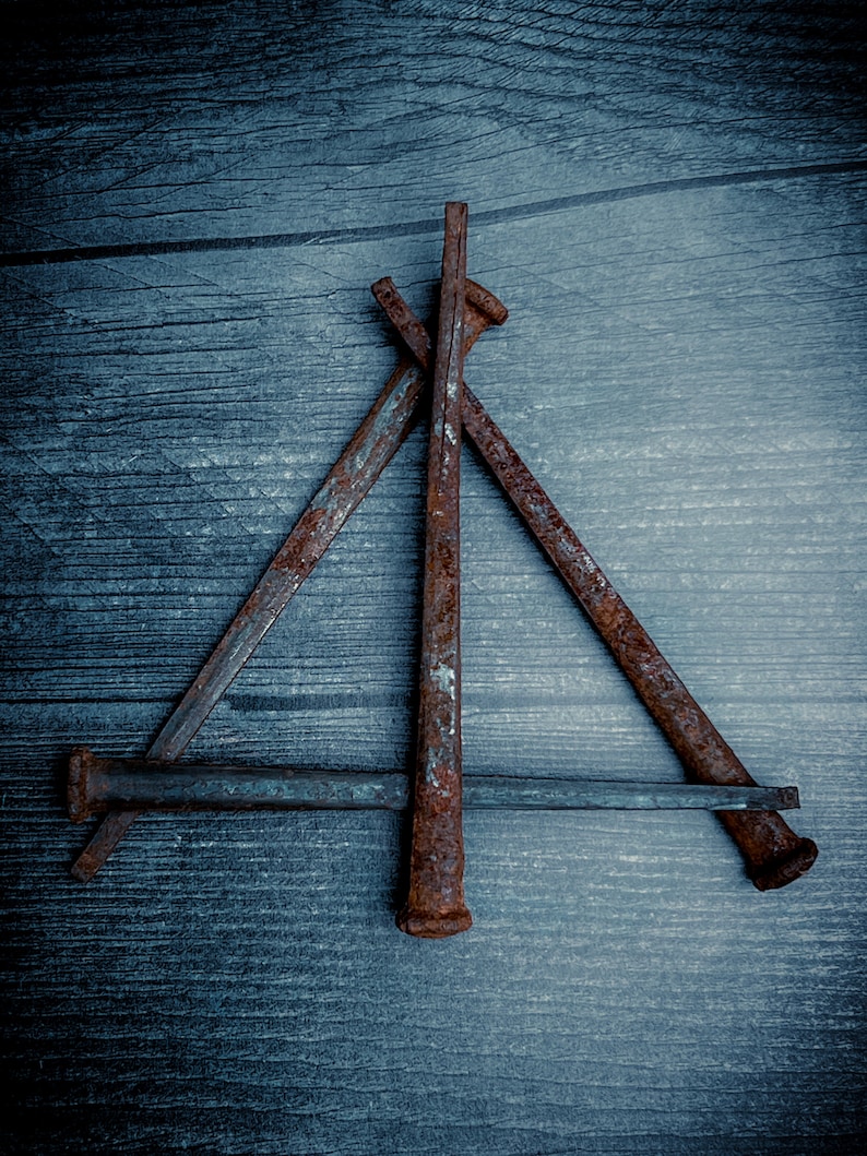 May include: A collection of rusty, weathered nails arranged on a dark blue wooden surface. The nails are positioned to form a geometric shape, showcasing their aged, textured appearance. The composition highlights the contrast between the metal and wood.