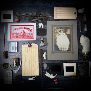 Puede incluir: Un surtido de artículos antiguos y vintage, que incluyen una fotografía enmarcada, una tarjeta de adivino, una etiqueta de dedo del pie, una pluma, dientes y pequeños viales. Los artículos están dispuestos sobre una superficie de madera oscura, creando una estética misteriosa e histórica.