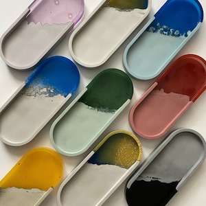 May include: Nine oval-shaped concrete trays with a variety of colored resin inlays. The trays are all different colors, including purple, yellow, blue, green, pink, and black.