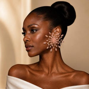 May include: A large, starburst-shaped statement earring featuring numerous pale pink, teardrop-shaped beads attached to thin, radiating gold-toned wire spokes. The earring covers the earlobe and extends outward in a circular, sunburst pattern.