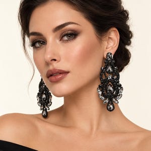 May include: A pair of long, ornate chandelier earrings featuring intricate black beadwork and faceted gray crystal accents in teardrop and marquise shapes. The earrings have a symmetrical, filigree-inspired design with a dark, metallic finish.
