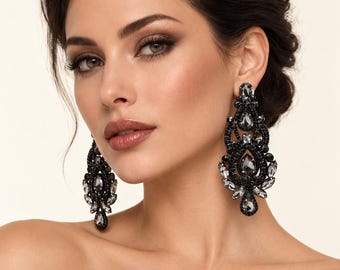 May include: A pair of long, ornate chandelier earrings featuring intricate black beadwork and faceted grey crystal accents in teardrop and marquise shapes. The earrings have a symmetrical, filigree-inspired design with a dark, metallic finish.