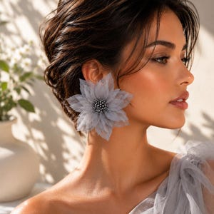 May include: A large, grey, multi-layered fabric flower earring featuring a cluster of small, dark grey beads at its center. The petals are made of a sheer, lightweight material with pointed edges, creating a full, dimensional floral shape.