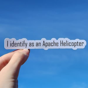May include: A white sticker with the text "I identify as an Apache Helicopter" against a blue sky background.