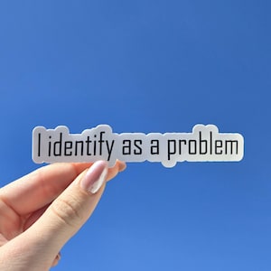 Puede incluir: Una pegatina blanca con el texto "I identify as a problem" en negro, sobre un cielo azul. La pegatina tiene forma rectangular redondeada.
