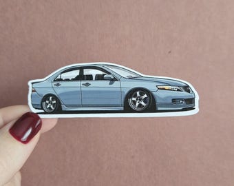 May include: A sticker featuring a light blue sedan with custom wheels. The car is depicted in a side profile, with a lowered suspension. The sticker has a white border and is held against a neutral background.