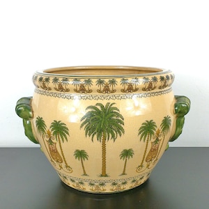 May include: A ceramic planter with green handles and a beige background. The planter is decorated with a repeating pattern of palm trees and small figures.
