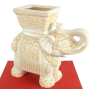 May include: Ivory-colored elephant planter with a square top, detailed with carved patterns. The elephant is standing on a red book, with another book below it that reads "Bunny Williams' Point of View".