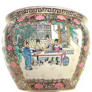 May include: A large, round ceramic planter with a detailed, hand-painted design. The planter features a scene of people in traditional clothing, with pink floral and gold accents. The rim has a geometric pattern.