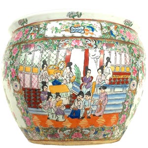 May include: A large, round, white ceramic planter with a hand-painted scene of people in traditional clothing. The planter is decorated with floral and geometric patterns in pink, green, and gold.
