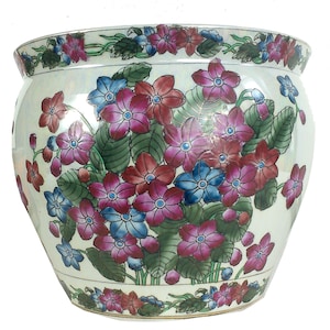 May include: A round ceramic planter featuring a glossy off-white finish decorated with a vibrant pattern of pink, red, and blue five-petaled flowers and green leaves. The design includes a floral border along the top rim and the base.