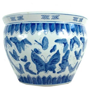 May include: A white and blue ceramic planter with a wide, rounded shape. The planter is decorated with blue butterfly motifs and floral patterns. The rim and base feature detailed blue designs, creating a decorative garden accent.