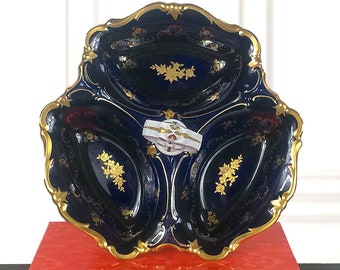 May include: A blue and gold porcelain serving dish with three sections. The dish is decorated with gold trim and floral patterns. The dish is sitting on a red book with the title "Wanderlust" printed on the cover.