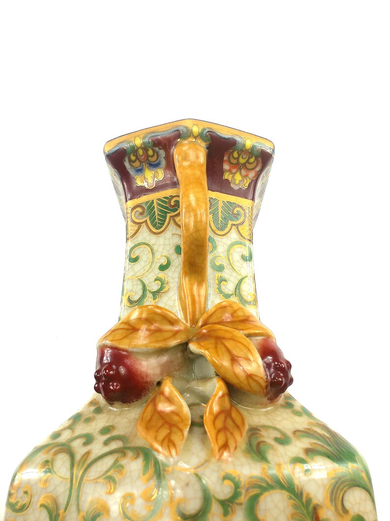 May include: A ceramic vase with a square base and a decorative handle. The vase is decorated with a floral pattern in shades of green, yellow, and red.