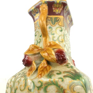 May include: A decorative ceramic vase with a yellow, green, and red floral design. The vase has a unique handle with a floral design and a square base.