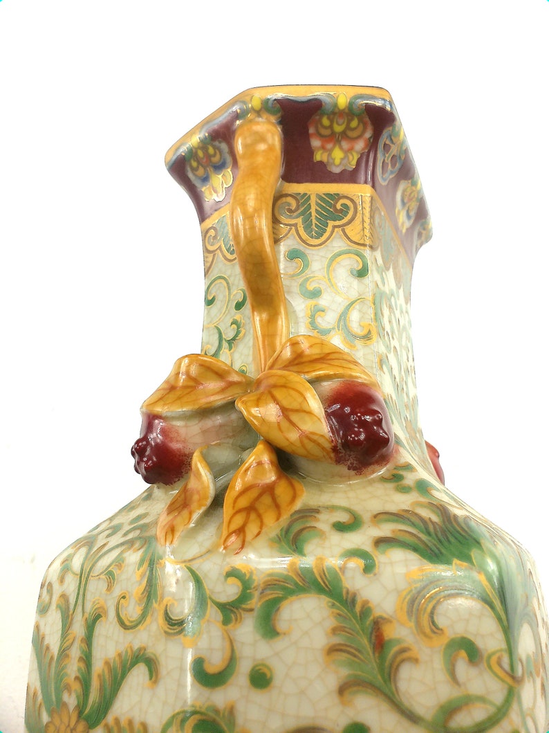 May include: A decorative ceramic vase with a yellow, green, and red floral design. The vase has a unique handle with a floral design and a square base.