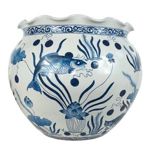 May include: A large, round ceramic planter featuring a white base with blue hand-painted illustrations of fish, lotus flowers, and aquatic plants. The vessel has a wide, scalloped rim and a decorative blue patterned border around the top edge.