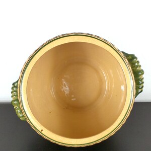 May include: A ceramic serving bowl with green and yellow accents. The bowl has two handles and is empty.