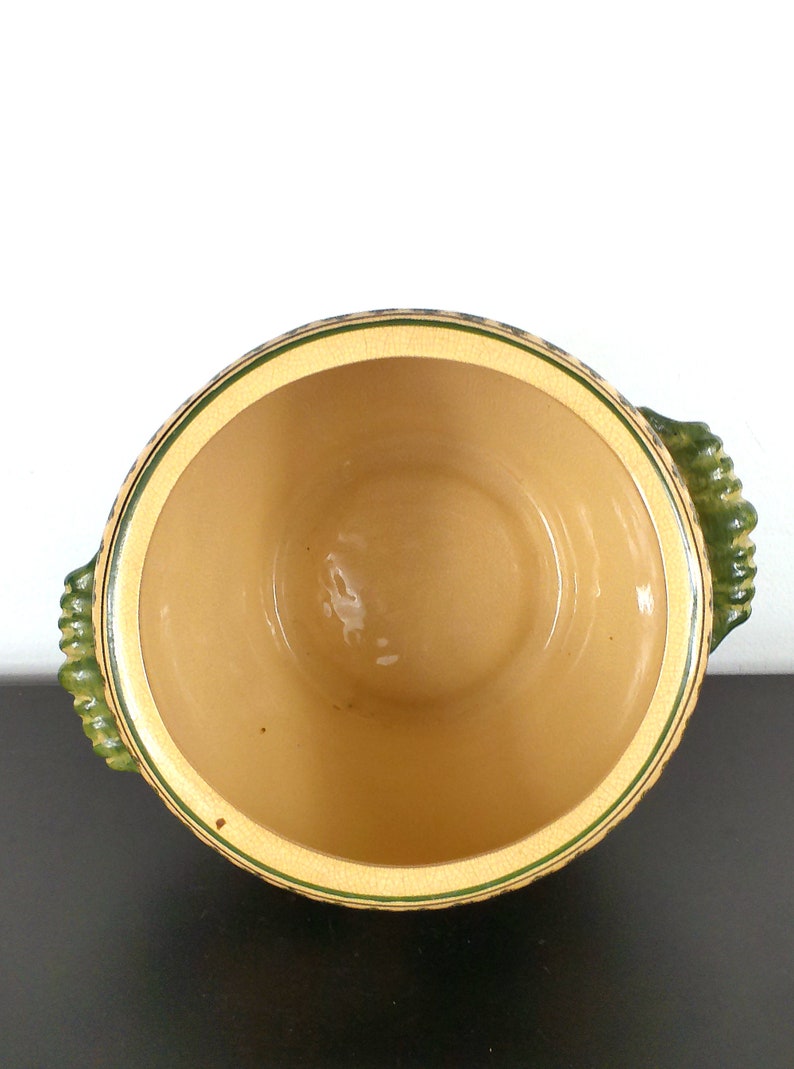 May include: A ceramic serving bowl with green and yellow accents. The bowl has two handles and is empty.