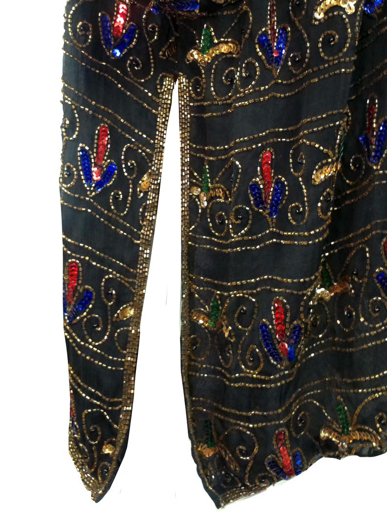 Pu&ograve; includere: Un scialle nero con paillettes con accenti dorati, rossi, blu e verdi. Lo scialle ha una fessura sul lato ed &egrave; decorato con un motivo floreale ripetitivo.