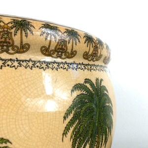 May include: A large, cream-colored ceramic planter with a crackled glaze. The planter is decorated with a repeating pattern of palm trees and a border of stars. The planter is perfect for adding a touch of tropical flair to any home.
