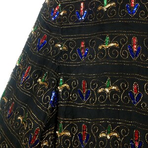 Pu&ograve; includere: Una giacca nera di paillettes con un motivo ripetuto di paillettes dorate, blu, rosse e verdi. Le paillettes sono disposte in un design floreale.