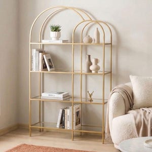 Könnte beinhalten: Ein goldfarbenes Metallregal mit Glasböden und einem bogenförmigen Oberteil. Die Regale beherbergen Bücher, dekorative Vasen und eine kleine Topfpflanze. Das Regal befindet sich in einem Wohnzimmer mit einem Teppich und einem Sofa.