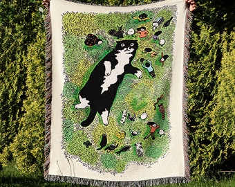 Puede incluir: Un tapiz tejido con un gato blanco y negro sobre un fondo verde, amarillo y marrón. El gato está rodeado de pequeñas figuras de personas y animales.