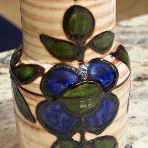May include: A ceramic vase with a floral design. The vase features a beige background with brown stripes and a flower design in blue and green. The rim and interior are brown.