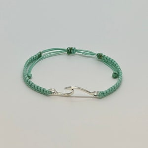 May include: A light green braided bracelet with a silver wave charm.