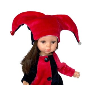 Puede incluir: Una muñeca con un traje de bufón rojo y negro con un gorro de bufón rojo y negro. El gorro tiene cascabeles en los extremos de las puntas.