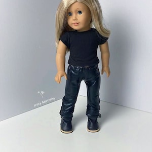May include: A doll wearing a black t-shirt and black pants. The doll has long blonde hair and blue eyes.