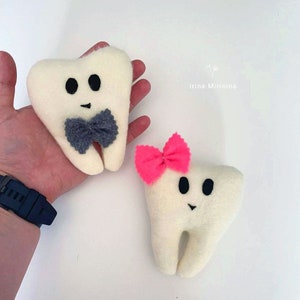 May include: Two plush white teeth toys, one with a gray bow tie and the other with a pink bow. The toys are on a white surface.  Irina Mirinina.