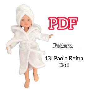 Peut inclure: Une poupée vêtue d'un peignoir et d'une serviette en éponge blancs, avec le texte "PDF Pattern 13" Paola Reina Doll". La poupée porte une robe à capuche avec une serviette assortie autour de la tête.