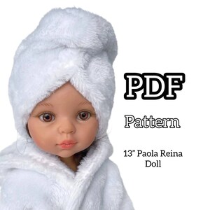Puede incluir: Una muñeca con una envoltura y toalla de spa de rizo blancas. La muñeca tiene ojos marrones y lleva una bata blanca. El texto "PDF Pattern" y "13" Paola Reina Doll" son visibles.