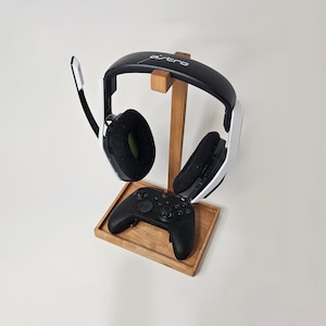May include: A wooden stand with a black and white gaming headset and a black controller. The headset has the word "ASTRO" printed on it.