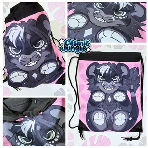 May include: A pink drawstring bag with a black furry creature with white markings on a pink background. The creature has a black nose and white eyes. The bag has a black drawstring and black handles. The text "Cosmic Jungle" is printed on the bag.