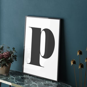 May include: A black and white print of the letter "p" in a bold, modern font. The print is framed in a black frame and is hanging on a teal wall.