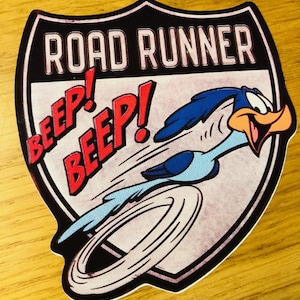 May include: A black and white Road Runner sticker with a red "Beep! Beep!" and the words "Road Runner" in white. The Road Runner is blue and white and is running in a circle.