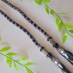 May include: Two black and silver braided cords with silver metal beads and crow head charms at the ends.