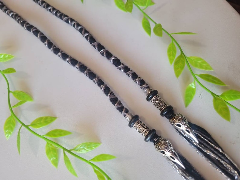 May include: Two black and silver braided cords with silver metal beads and crow head charms at the ends.