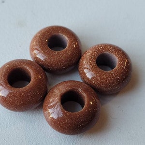 Könnte beinhalten: Vier braune donutförmige Perlen mit einem Loch in der Mitte. Die Perlen bestehen aus einem gesprenkelten Material.