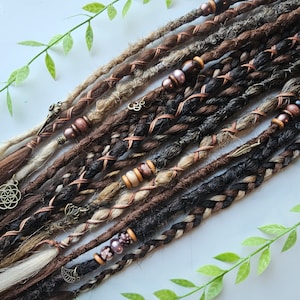 Puede incluir: Un conjunto de rastas sintéticas marrones, negras y rubias con detalles de alambre de cobre y cuentas. Las rastas están decoradas con dijes y cuentas de varios colores y estilos.