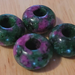 May include: Four green and purple gemstone beads with a hole in the centre. The beads are round and have a mottled appearance.