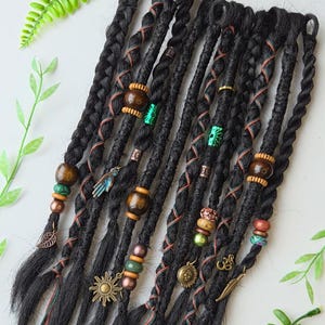 Peut inclure: Un ensemble de dreadlocks synthétiques noires avec des perles et des breloques brunes, vertes et dorées. Les dreadlocks sont attachées avec de la ficelle rouge et verte.