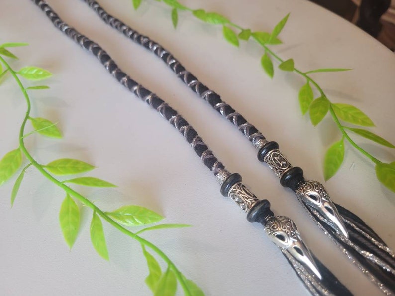 May include: Two black and silver braided cords with silver bird head charms at the ends. The cords are braided with a silver thread.