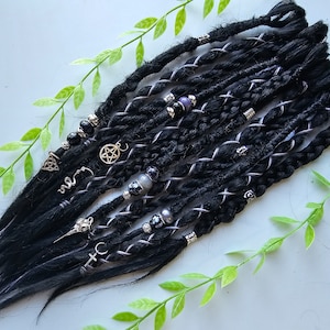 Könnte beinhalten: Schwarze synthetische Dreadlocks mit silbernen und schwarzen Perlen, Charms und Draht-Akzenten. Die Dreadlocks sind in einer Reihe auf einer weißen Oberfläche angeordnet.