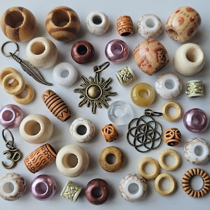 May include: Assortment of colourful wooden beads, some with intricate designs, and metal charms, including a large gold charm with a four-pointed star design. The beads are arranged on a white surface.